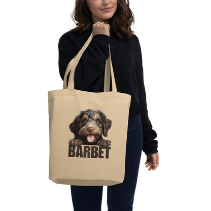 Nainen pitelee kangaskassia, jossa on barbet-koira ja ruskea teksti "barbet".