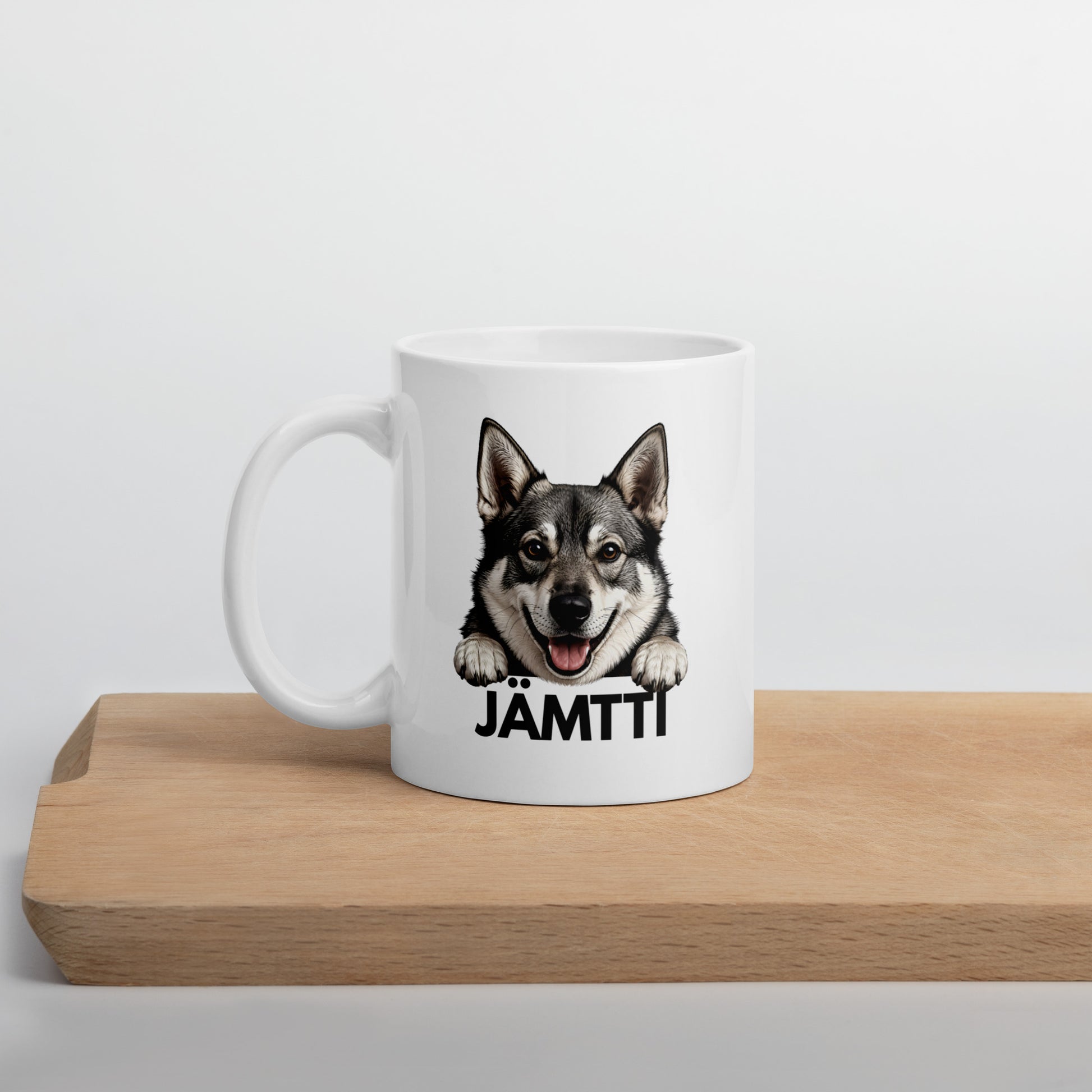 Valkoinen jämtlanninpystykorva-aiheinen muki "jämtti"-tekstillä, puisen laudan päällä kuvattuna.