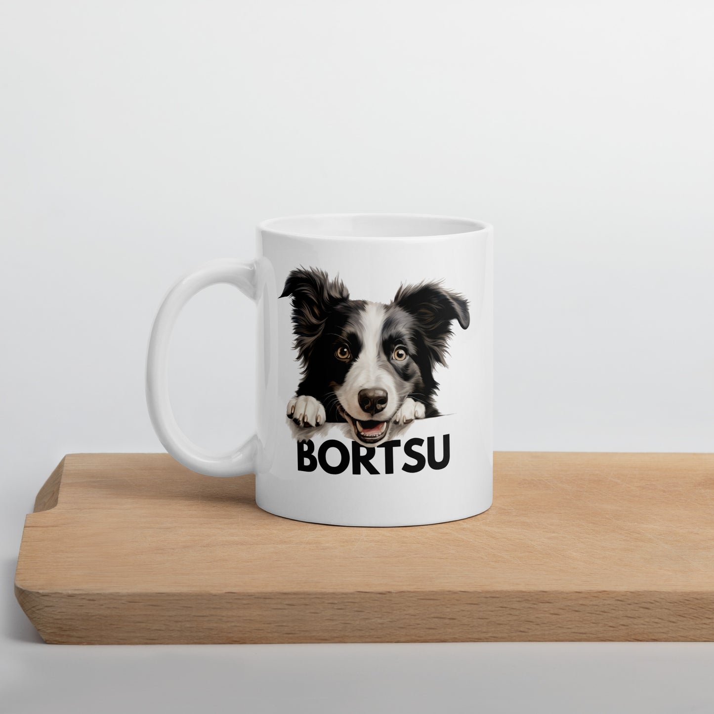 Valkoinen muki, jossa bordercollien kuva ja tumma teksti "bortsu" leikkuulaudan päällä kuvattuna.