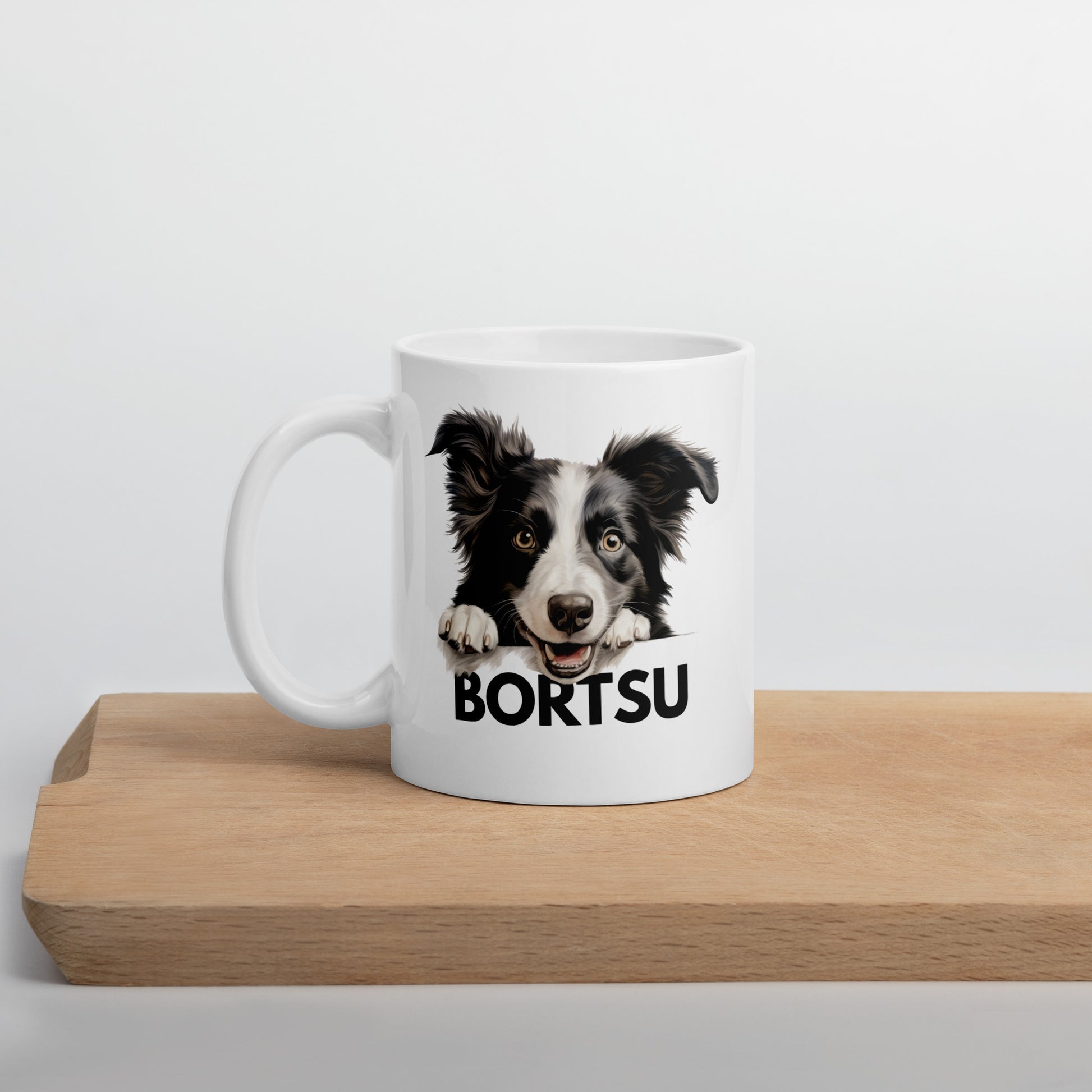 Valkoinen muki, jossa bordercollien kuva ja tumma teksti "bortsu" leikkuulaudan päällä kuvattuna.