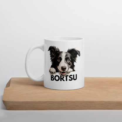 Valkoinen muki, jossa bordercollien kuva ja tumma teksti "bortsu" leikkuulaudan päällä kuvattuna.