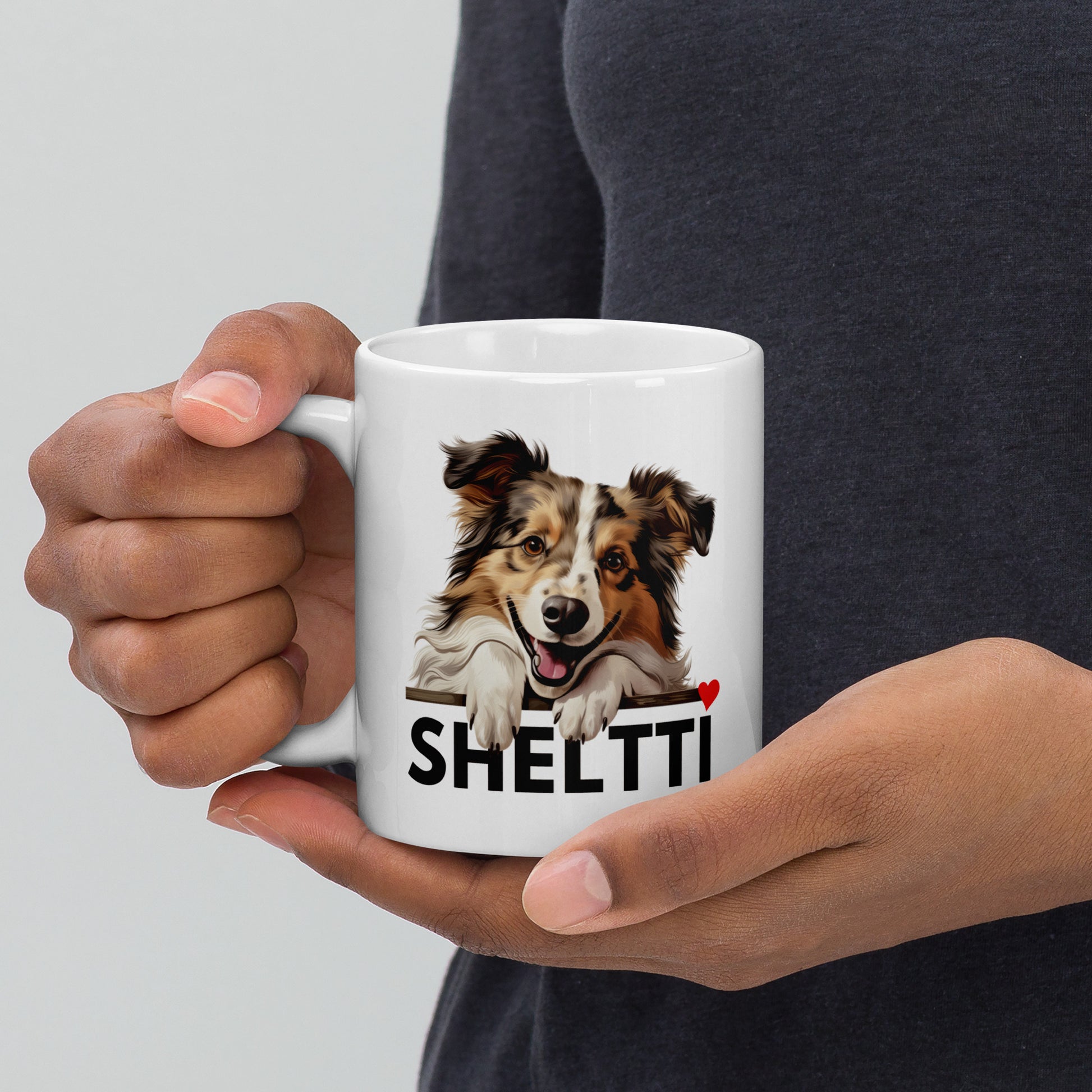 Mies kädessään shetlanninlammaskoiramuki, jossa tumma teksti "sheltti" ja sydän.