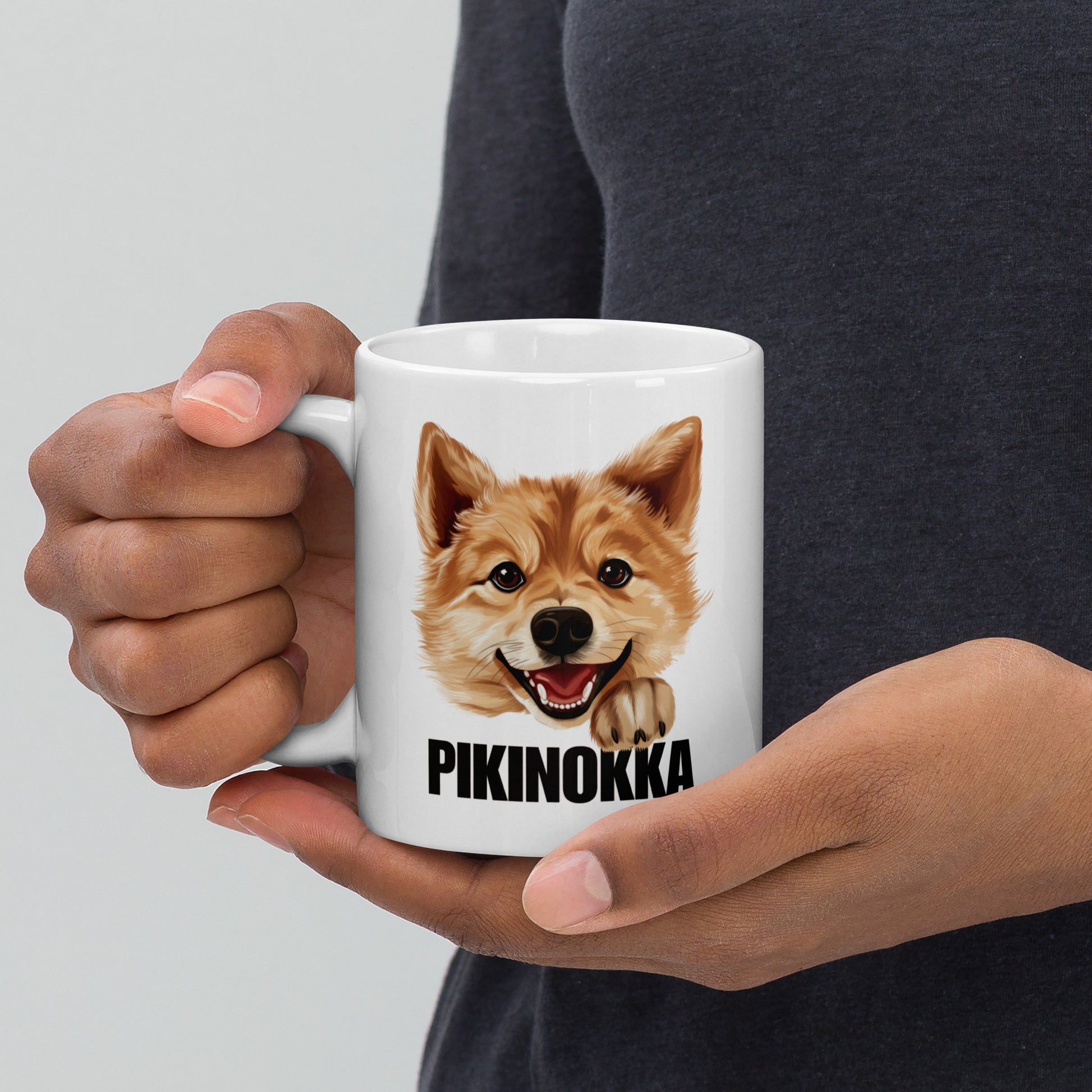 Mies pitelee käsissään valkoista mukia, jossa on suomenpystykorvan kuva ja musta teksti "pikinokka".