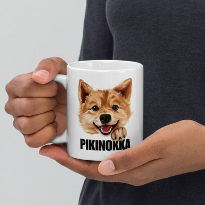 Mies pitelee käsissään valkoista mukia, jossa on suomenpystykorvan kuva ja musta teksti "pikinokka".