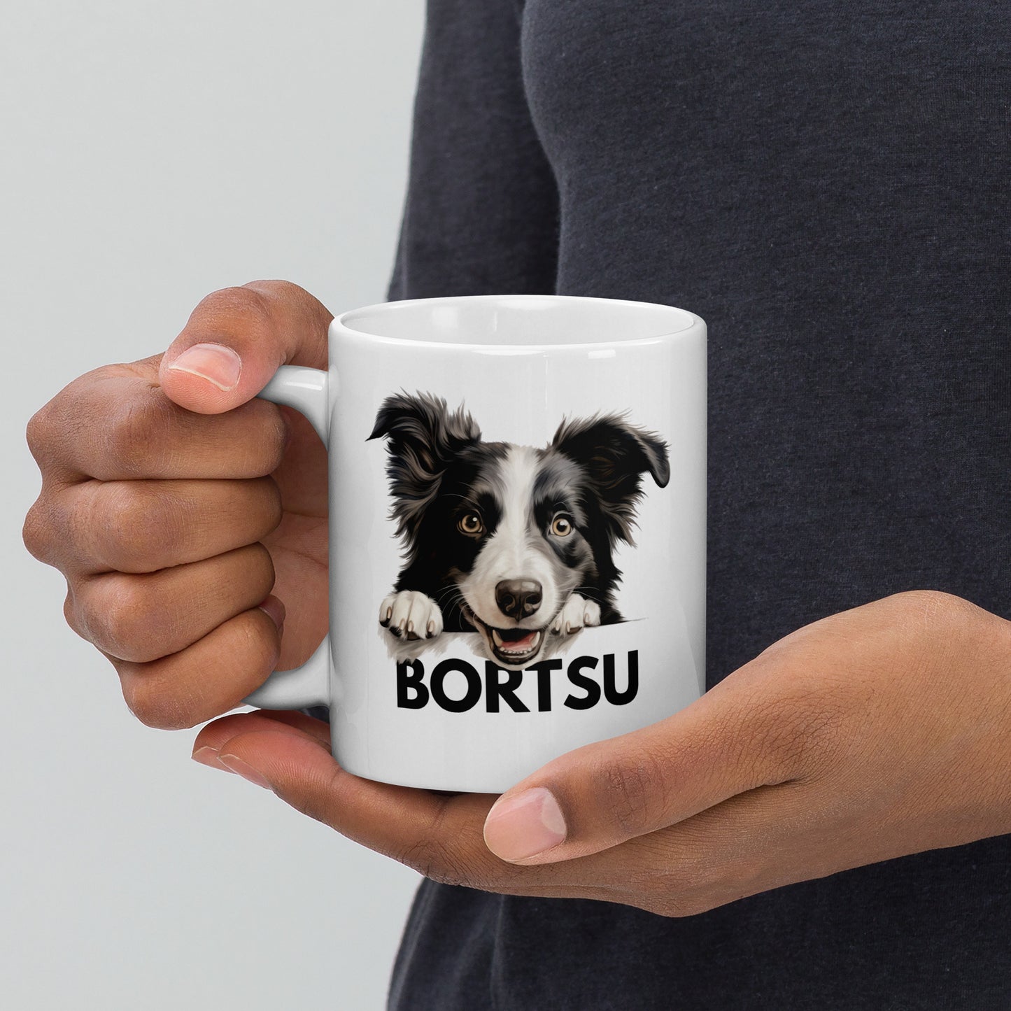 Mies kädessään valkoinen muki, jossa bordercollie-koiran kuva ja teksti "bortsu".