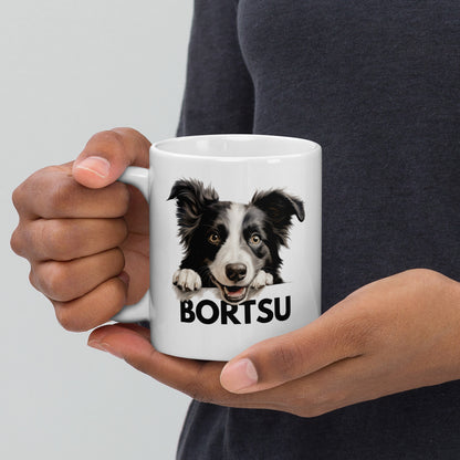 Mies kädessään valkoinen muki, jossa bordercollie-koiran kuva ja teksti "bortsu".