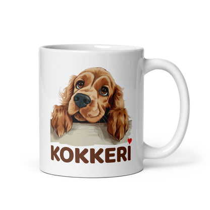 Lähikuva valkoisesta mukista, jossa on kurkkaavan cockerspanielin kuva ja teksti "Kokkeri" punaisella sydämellä.