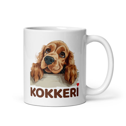Lähikuva valkoisesta mukista, jossa on kurkkaavan cockerspanielin kuva ja teksti "Kokkeri" punaisella sydämellä.