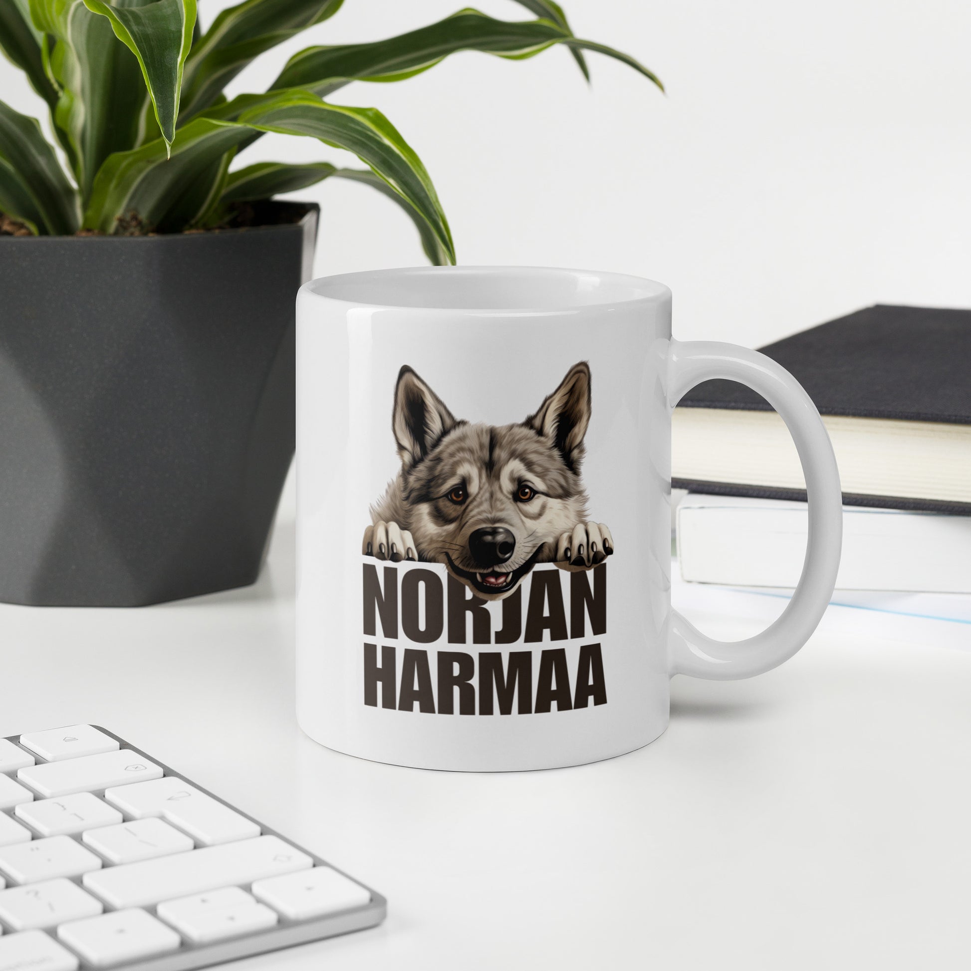 Pöydällä valkoinen muki, jossa harmaa norjanhirvikoira ja teksti "NORJANHARMAA".