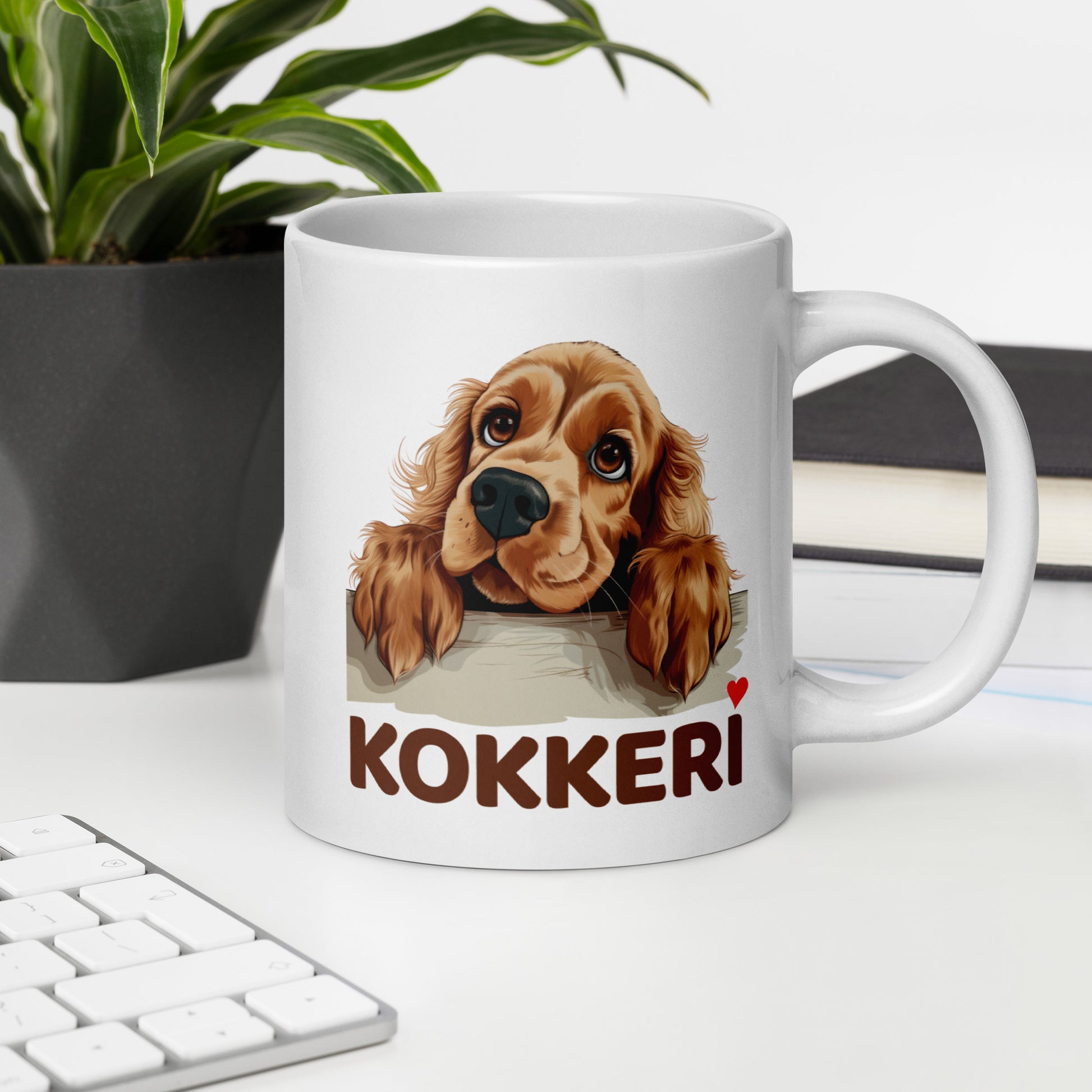 Työpöydällä valkoinen muki, jossa cockerspanielin kuva ja teksti "kokkeri" punaisella sydämellä varustettuna.